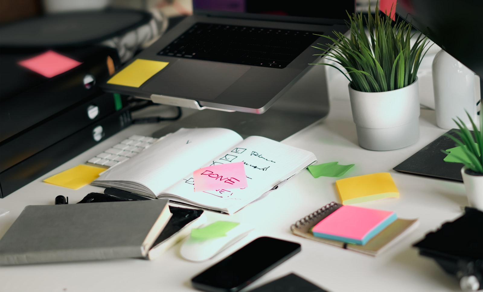 A cluttered desk covered in sticky notes, a laptop, and scattered office supplies